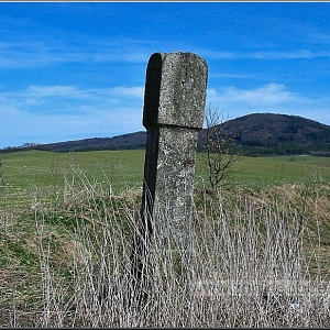 Torzo božích muk při staré cestě z Plání do Hyršova. Vlevo v pozadí na horizontu s náletem samoty stávaly, vpravo vrch Jezvinec (739 m).