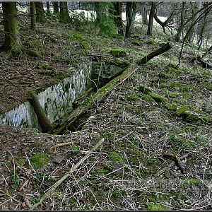 Betonová nádrž na vodu z pohledu od osamoceně stojící usedlosti u potoka.